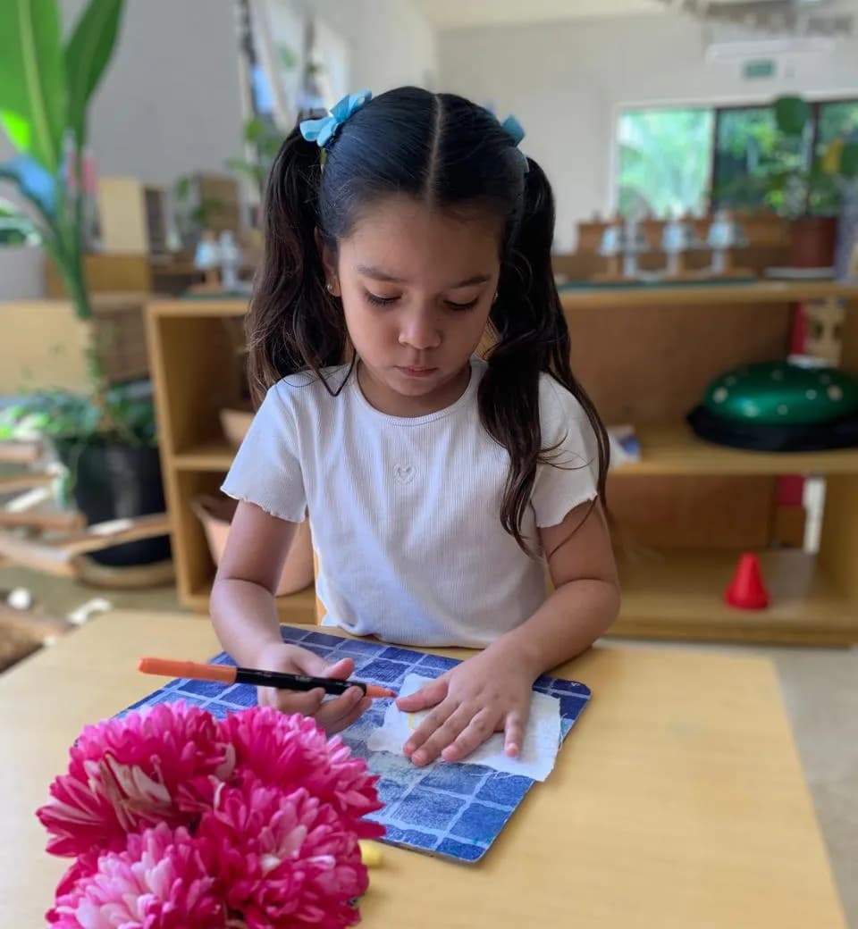 Niña concentrada en su trabajo junto a un florero con flores rosas